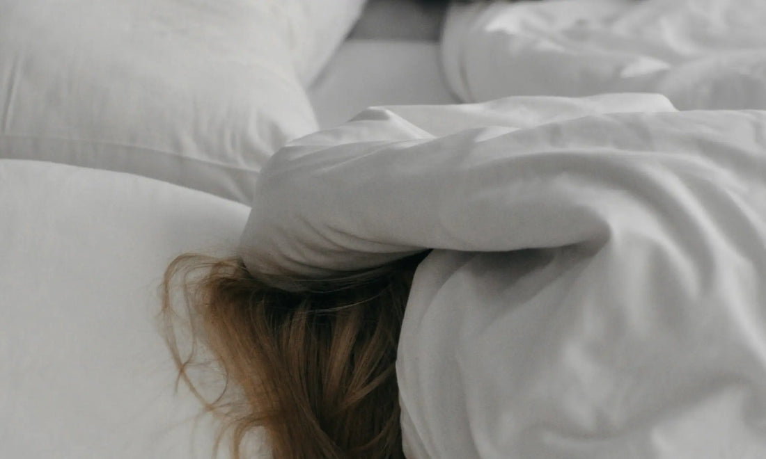 Person lying in bed with face hidden under a pillow, representing the struggle to stop thinking about work at night