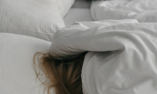 Person lying in bed with face hidden under a pillow, representing the struggle to stop thinking about work at night