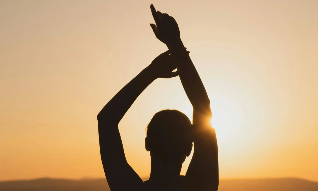 Person silhouetted at sunset with arms raised practising vagus nerve exercises for stress relief