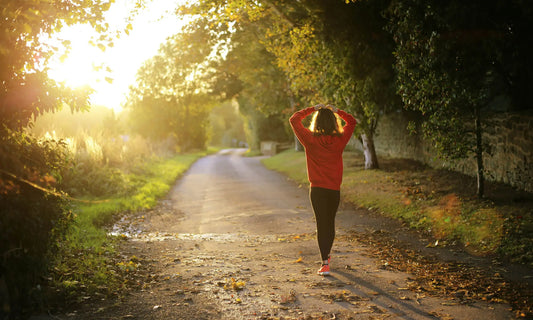 Person walking along a sunny tree-lined path with hands on head, representing a burnout recovery plan and taking steps forward