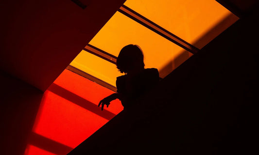 Person silhouetted against a deep orange background with head down, representing end-of-year burnout and emotional exhaustion in December