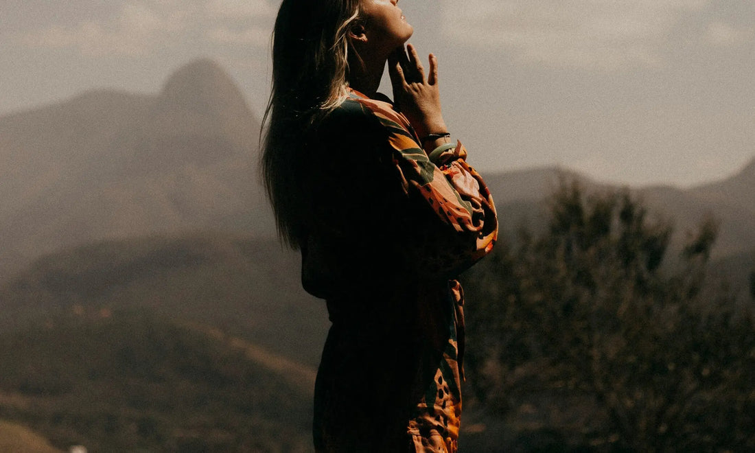 Person standing in a misty mountain landscape with hand raised to face, representing a moment of calm using breathing exercises for stress at work