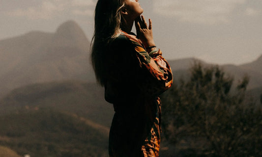 Person standing in a misty mountain landscape with hand raised to face, representing a moment of calm using breathing exercises for stress at work