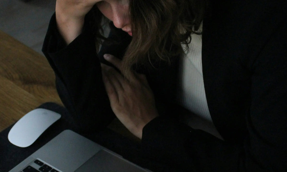 Person in dark clothing at a desk with hand on chest in a stress response, representing the signs of corporate burnout before it's too late