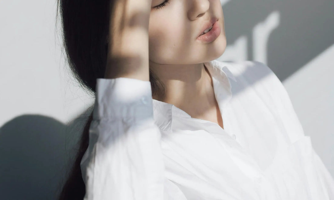 Person in a white shirt with head tilted back and eyes closed in soft light, representing learning how to switch off after work and decompress