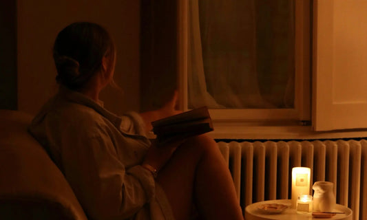 Person sitting alone by a window at night reading by candlelight, representing the Sunday scaries and the feeling of dread before the working week