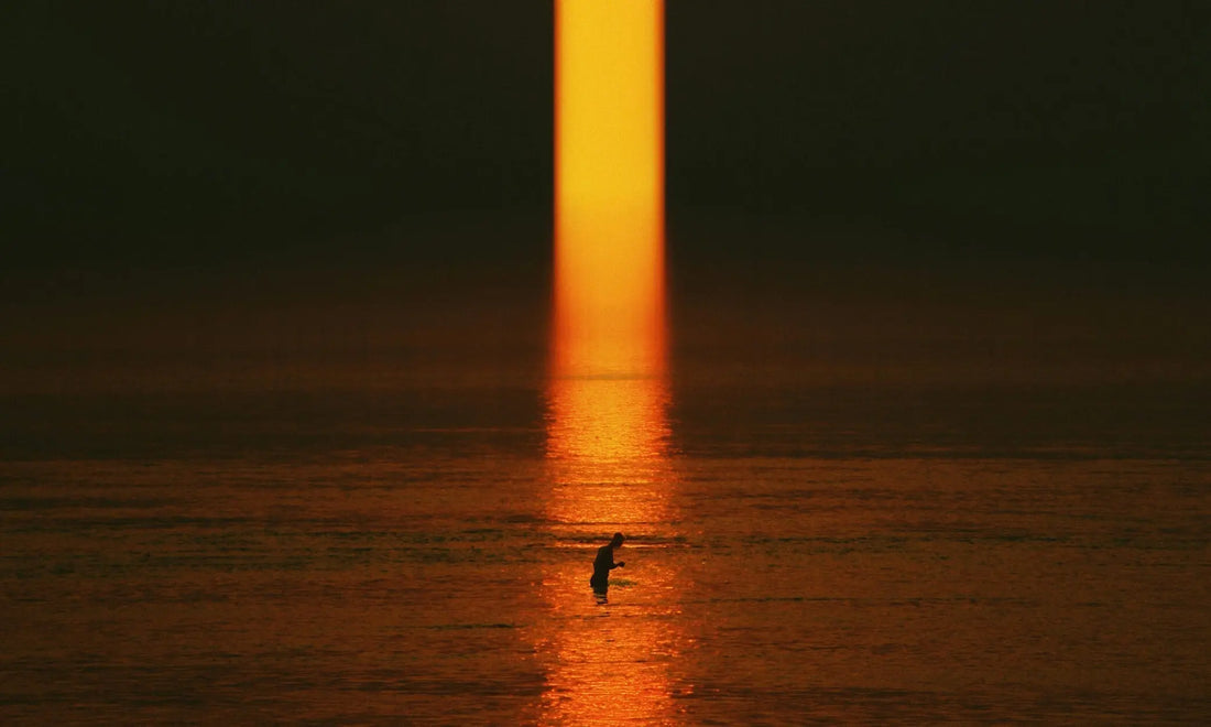 Person standing alone in calm water at sunrise, representing a gentle morning routine for burnout recovery and starting the day slowly
